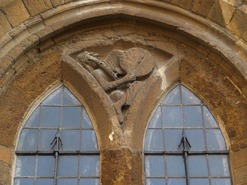 Higham Ferrers, England: Parish Church of St Mary the Virgin: carving on north side of tower (man playing flute and drum)